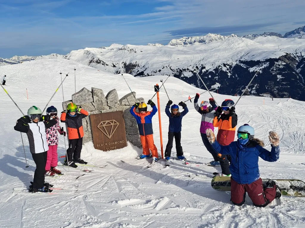 Kinder stehen vor einem Schild, das den Beginn der schwarzen Piste markiert. 